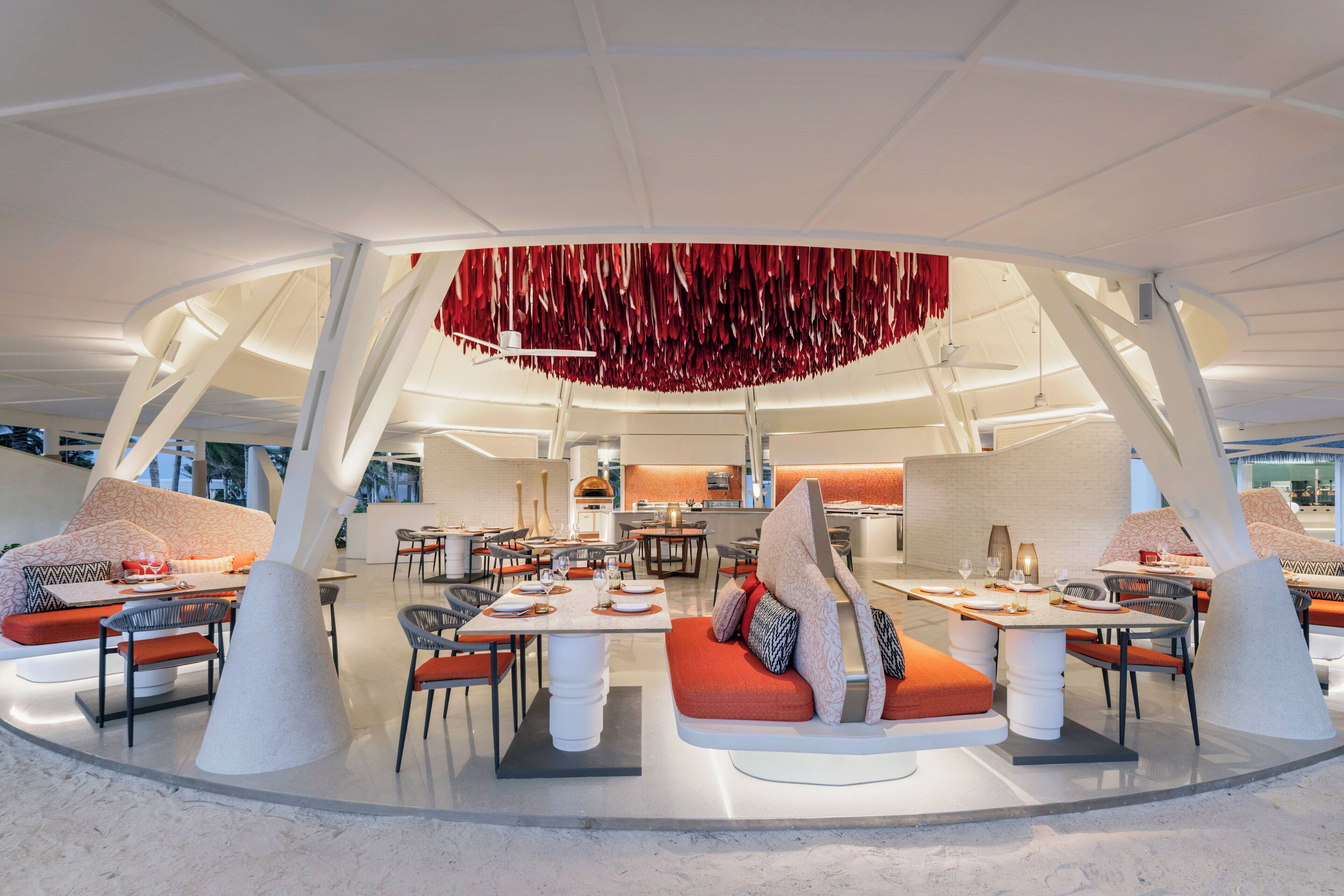 Un restaurante moderno con un área de comedor central, diversas opciones de asientos y un diseño de techo distintivo.