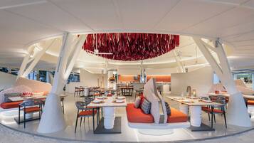 Un restaurante moderno con un área de comedor central, diversas opciones de asientos y un diseño de techo distintivo.