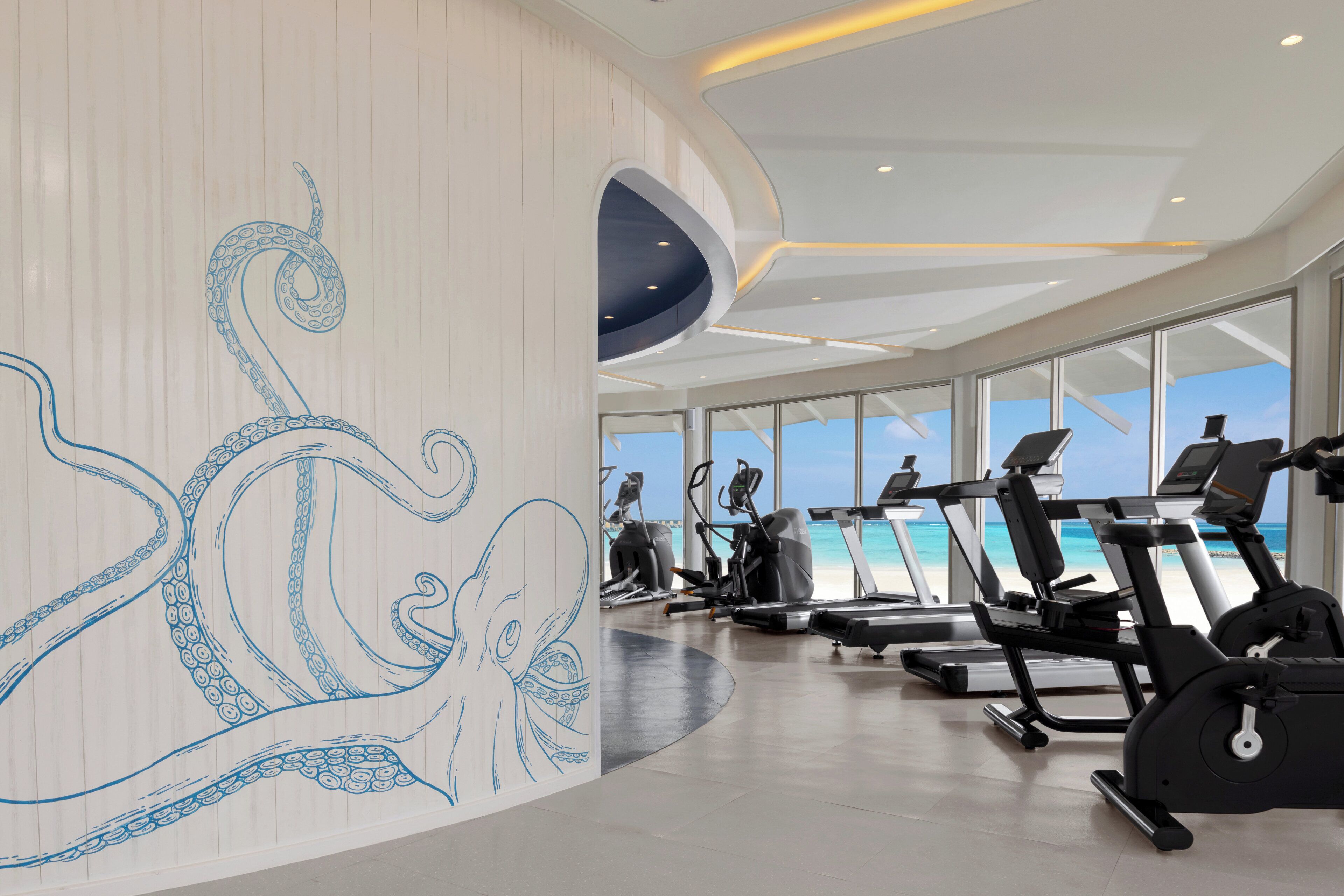 A gym with exercise equipment and a large wall mural of an octopus.