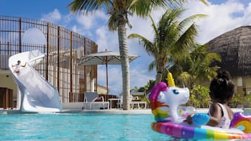 A pool area with a water slide, lounge chairs, and palm trees.