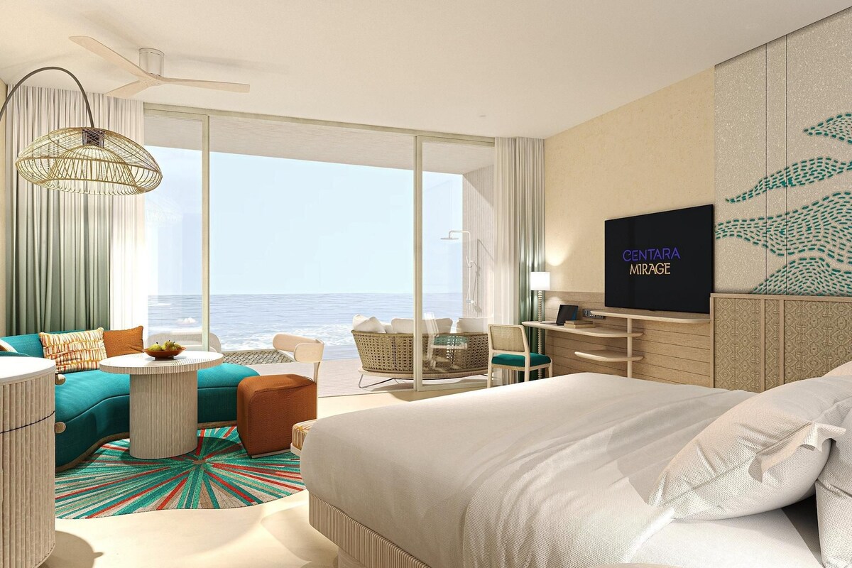 Una camera d'albergo con un letto grande, una TV, un balcone vista mare e una zona con un tavolo e sedie.