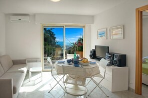 A modern living room with a sofa, a dining table with chairs, a TV, and a balcony with a view.