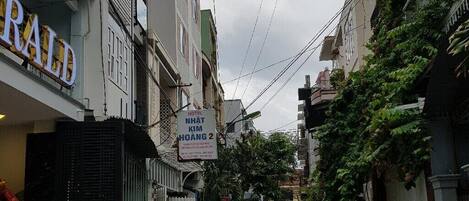 A narrow street with a hotel named "NHAT KIM HOANG 2" on the left, a "RALPH" store on the right, and motorcycles parked along the sides.