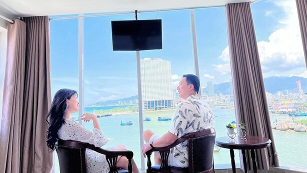 A room with a large window offering a city view, a flat-screen TV mounted on the wall, and two chairs facing each other.