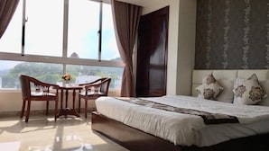 A hotel room with a large bed, a dining table with chairs, and a view of the outdoors through the window.