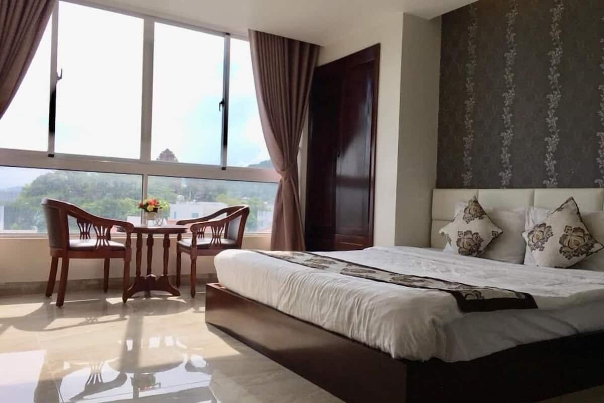 Ein Hotelzimmer mit einem großen Bett, einem Esstisch mit Stühlen und Blick ins Freie durch das Fenster.