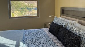 Une chambre à coucher avec un lit, une table de chevet, une lampe et une fenêtre donnant sur la montagne.