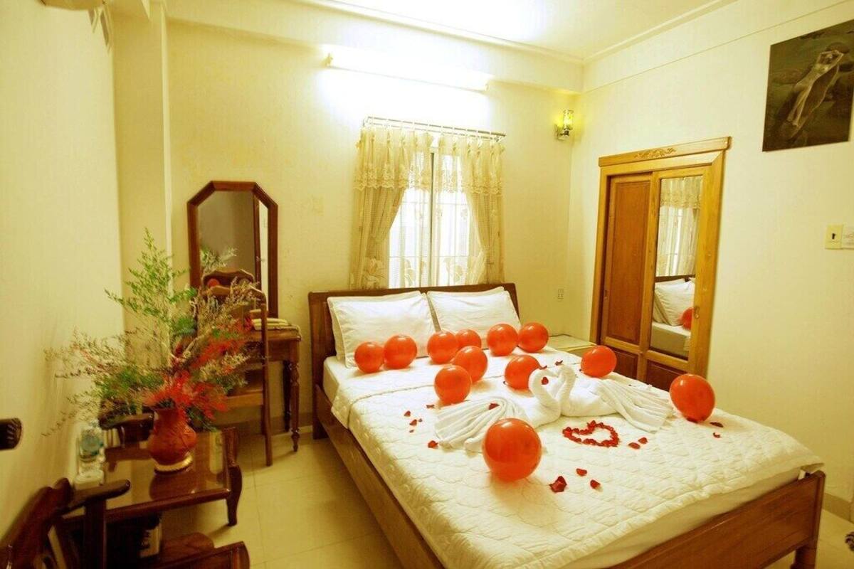 Quarto de hotel com cama, espelho, janela com cortinas e luminária fixada na parede.