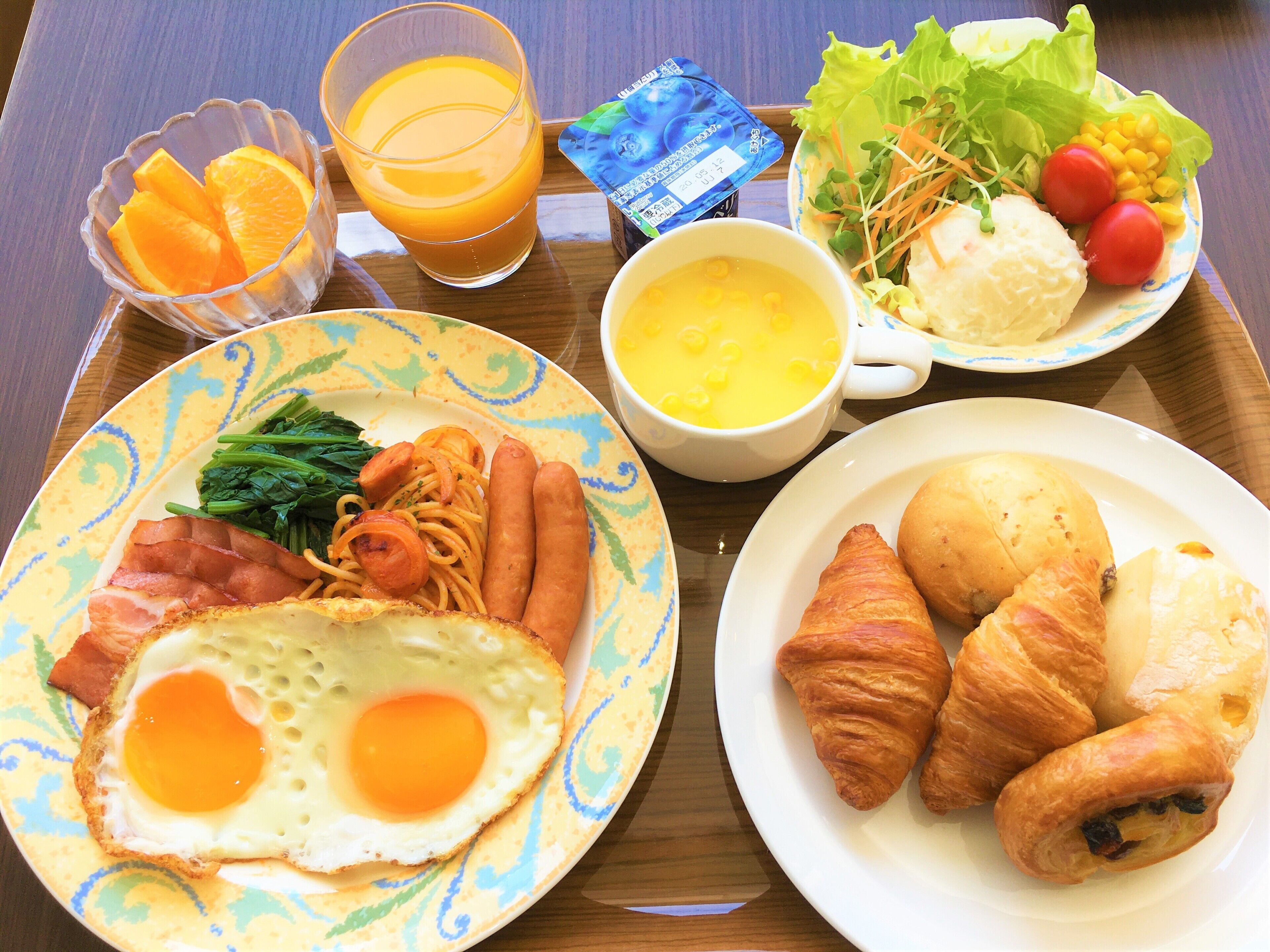 Bandeja de desayuno con huevos, salchichas, jamón, vegetales y cruasanes.