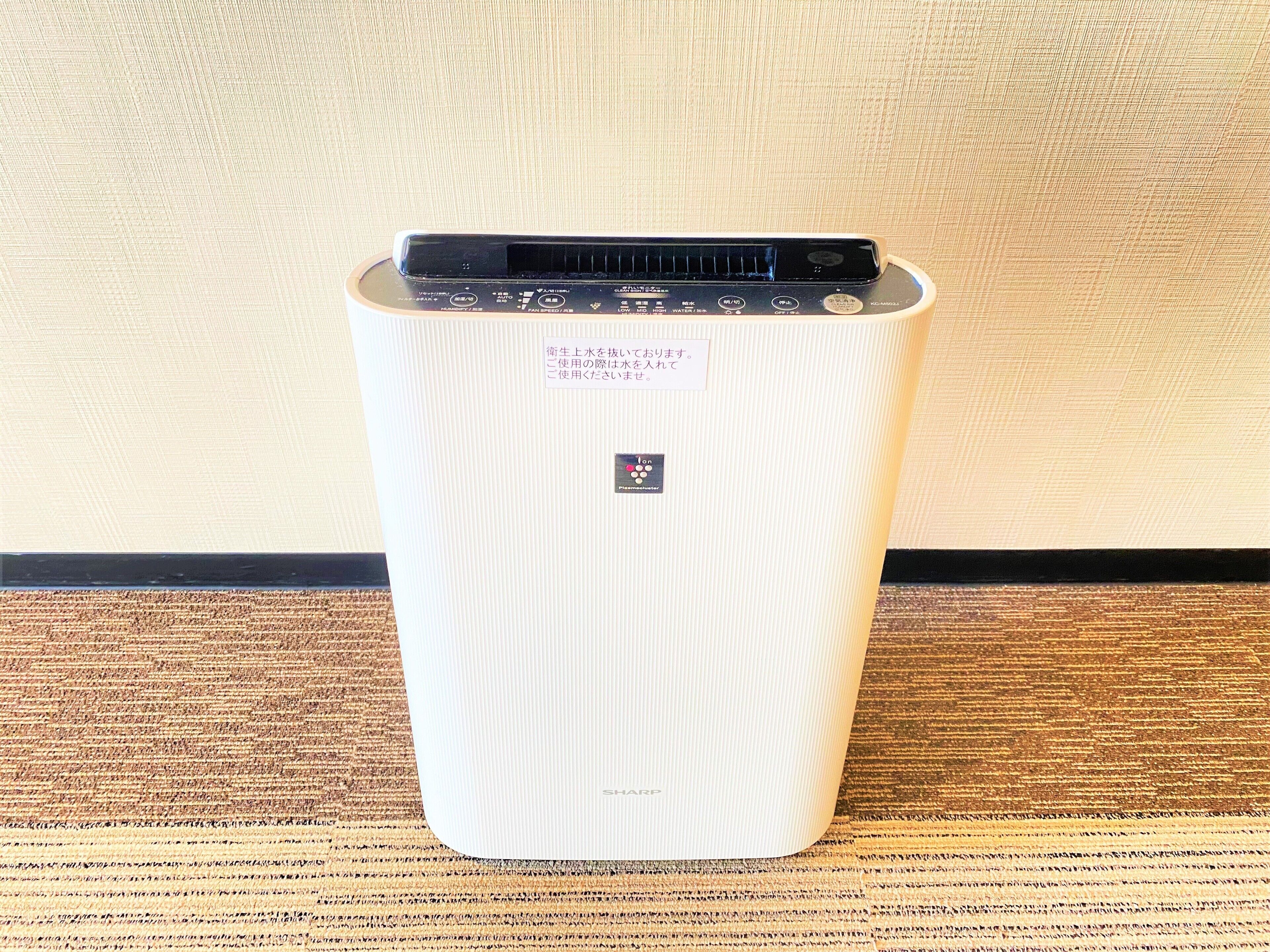 A white, ribbed, cylindrical device with a control panel on top, placed on a textured surface against a plain wall.