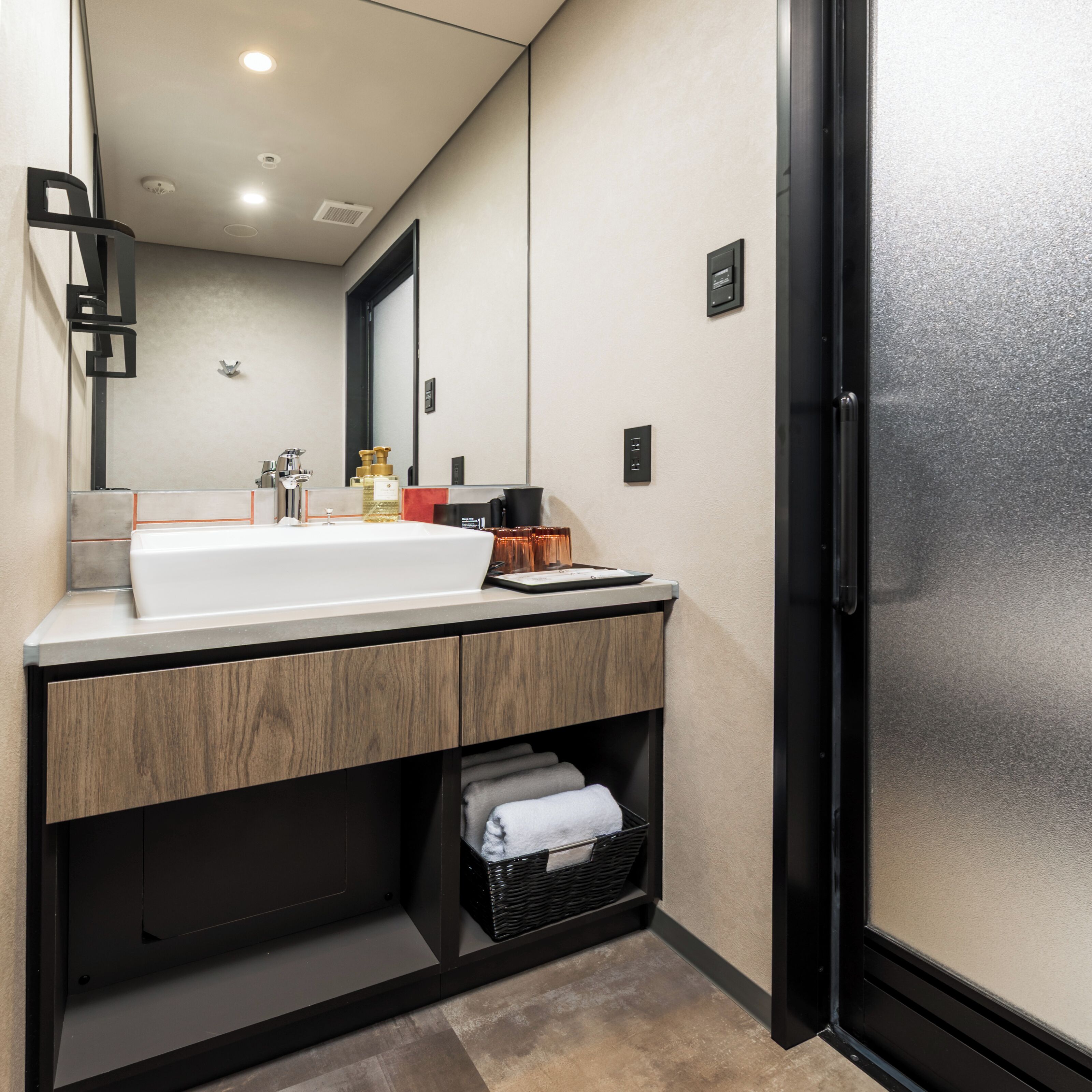 Un baño moderno con un lavamanos grande, tocador de madera y un espejo. Cuenta con un perchero y una cesta debajo del tocador.