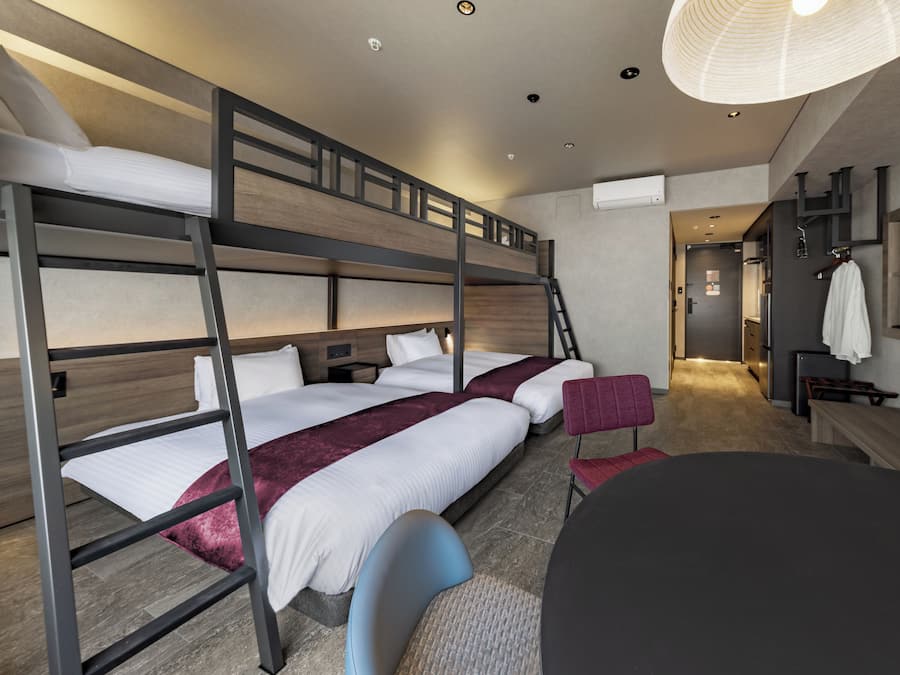 Ett hotellrum med våningssängar, ett skrivbord, en stol och ett stort fönster.