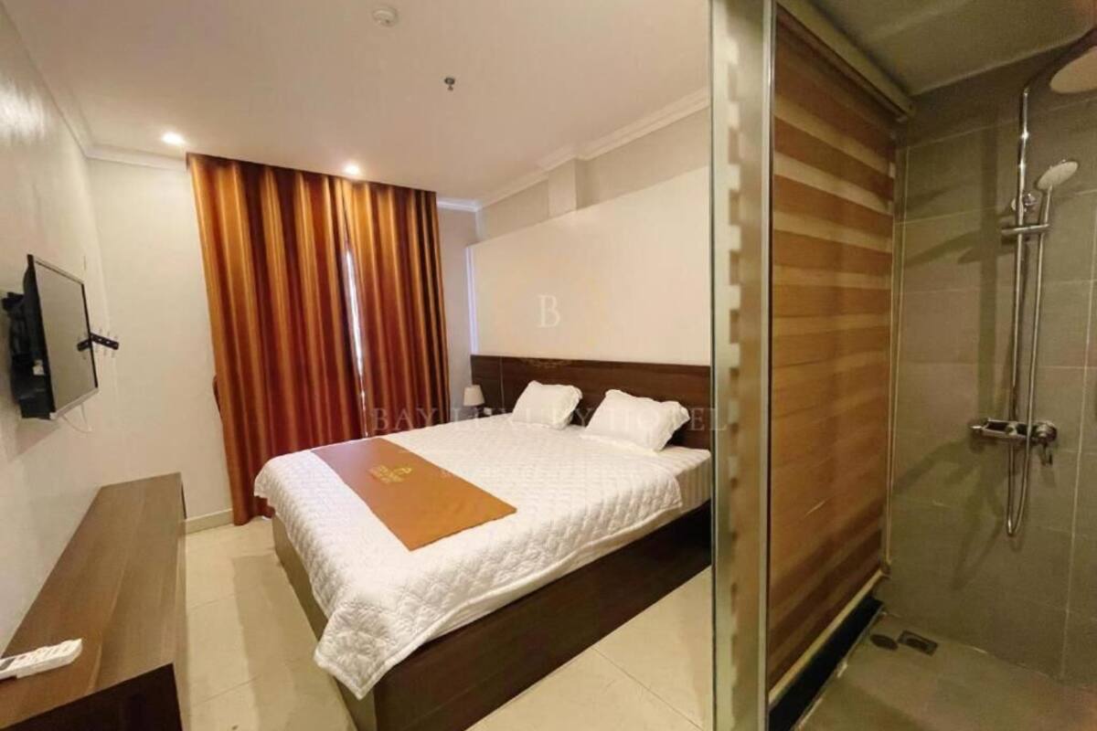 A hotel room with a bed, a wooden headboard, a glass shower enclosure, and a TV on a stand.