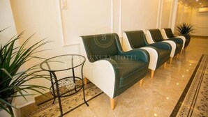 A lobby with a row of green sofas, a glass table, and a patterned rug. - Tien Thinh Hotel Ha Long- by Bay Luxury (Hong Gai)