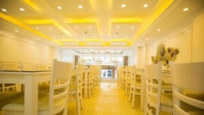 A hotel dining area with white chairs and tables, a central walkway, and a ceiling with recessed lighting. - Tien Thinh Hotel Ha Long- by Bay Luxury (Hong Gai)