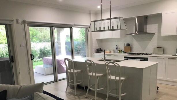 A modern kitchen with a central island, white cabinetry, and a dining area with white chairs. - Hawks Nest - Magic Square Location (Hawks Nest)