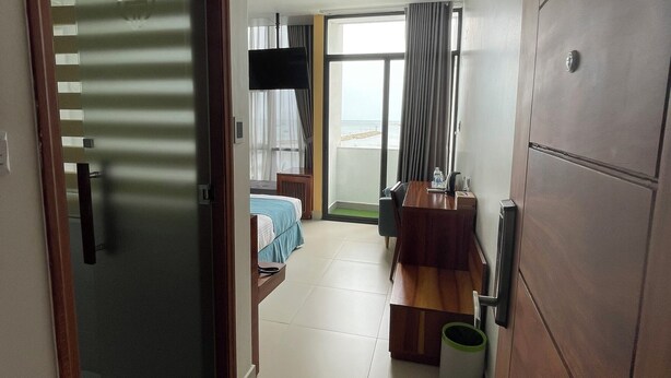 Une chambre d’hôtel avec un lit, un bureau, une chaise, une télévision et une vue sur la plage.