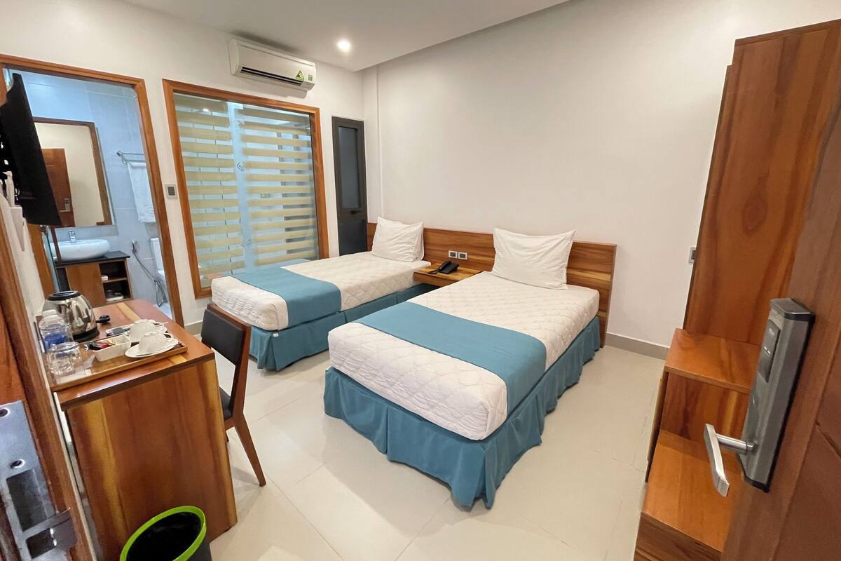 A hotel room with two beds, a desk with a telephone, a mirror, and an air conditioning unit.