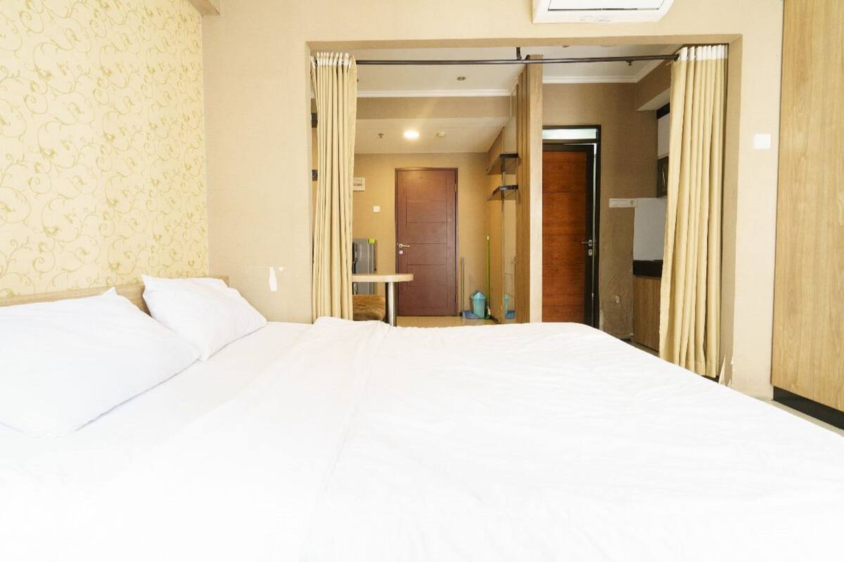 A hotel room with a large bed, a wardrobe, a door leading to a bathroom, and a small table with a chair.