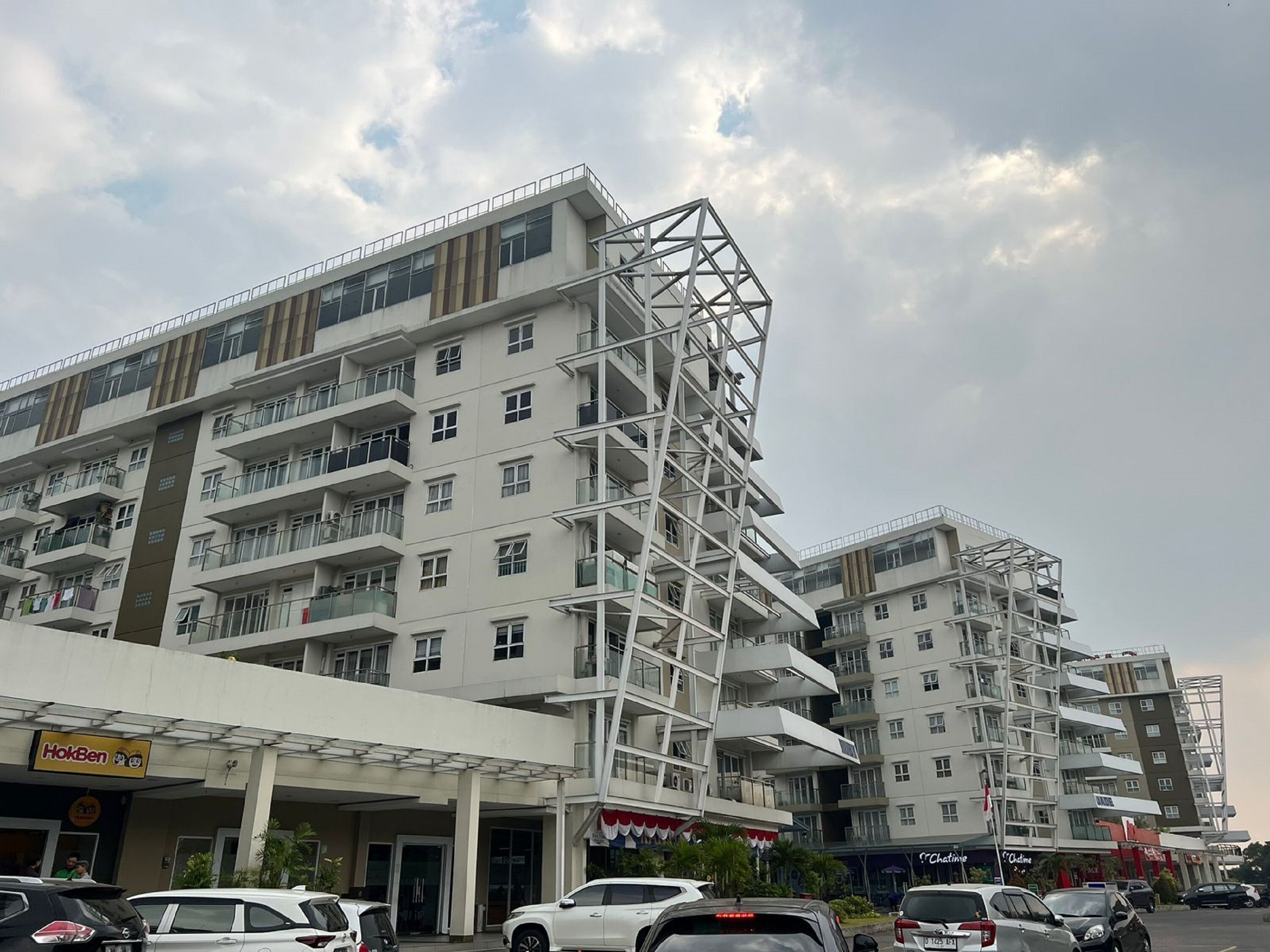 A multi-story hotel with balconies, a parking lot, and a visible restaurant named 'HokBen'.