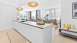 A modern kitchen with white cabinetry, a central island, and pendant lighting. - Welcome to your seaside sanctuary at Magnoli Palm Beach! (Gold Coast)