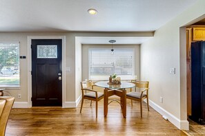 A dining area with a round glass table, four chairs, a dark wooden door, and a window with blinds.