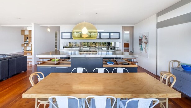 Een moderne keuken met een centraal eiland, een eetgedeelte met een houten tafel en stoelen, en een zithoek met een bank en planken.