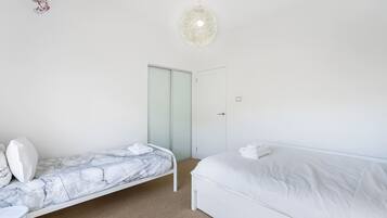 A bedroom with a single bed, a smaller bed with a marble headboard, a white wardrobe, and a hanging light fixture.