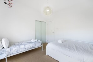 A bedroom with a single bed, a smaller bed with a marble headboard, a white wardrobe, and a hanging light fixture. - Getaway Hideaway-close to beach Sleeps-8 (Opossum Bay)