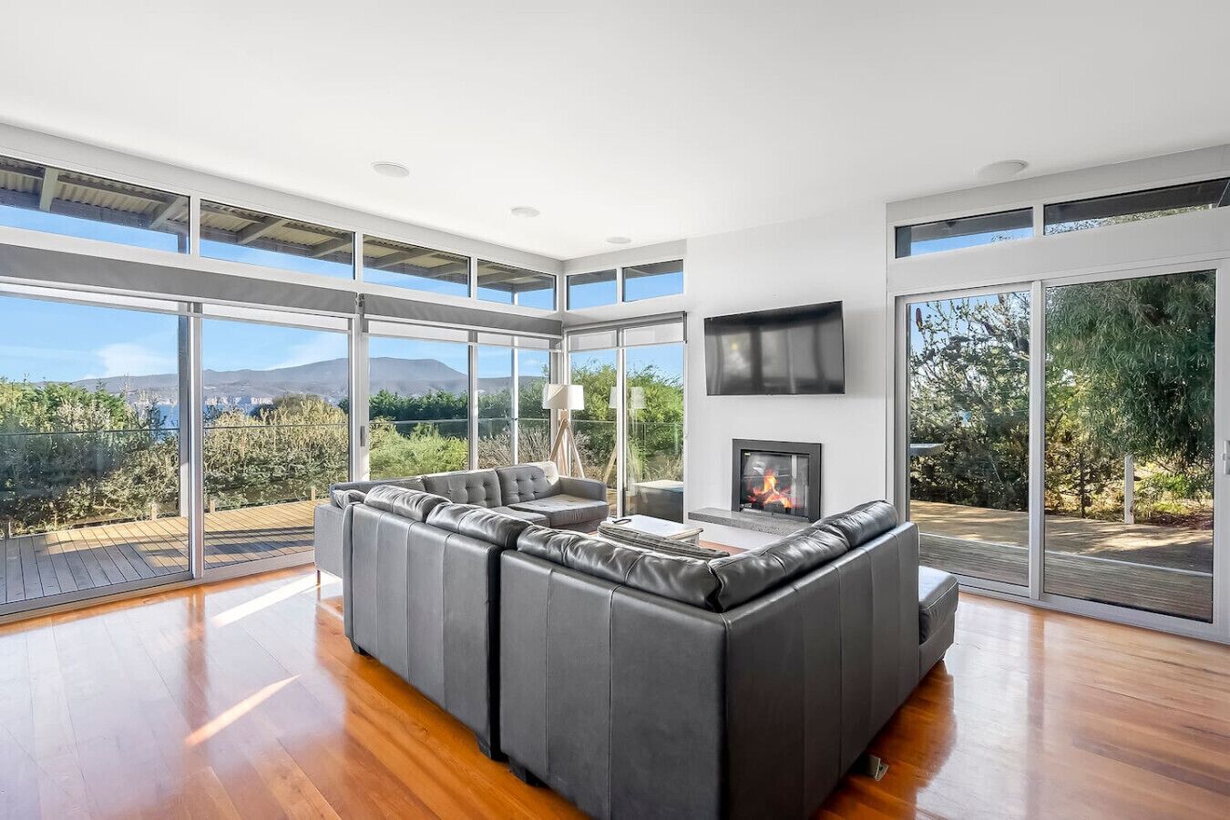 Una sala moderna con un amplio sofá seccional, una chimenea y amplias puertas de vidrio que dan a un paisaje exterior panorámico.