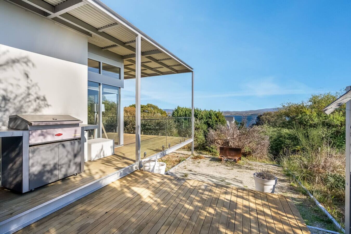 A modern house with a wooden deck, a barbecue grill, and a view of the sea.