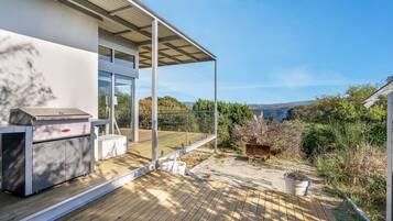 A modern house with a wooden deck, a barbecue grill, and a view of the sea.