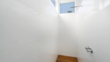 Een moderne douche met een houten vloer, witte wanden en een dakraam.