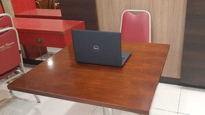 Una mesa de madera con una computadora portátil, sillas rojas y un armario rojo en una habitación con piso de baldosas.