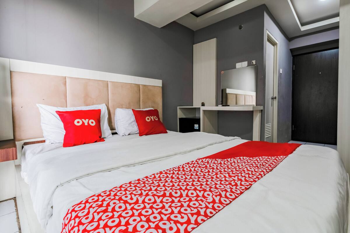 Una habitación de hotel moderna con una cama grande, un cabecero, un armario y una estantería.
