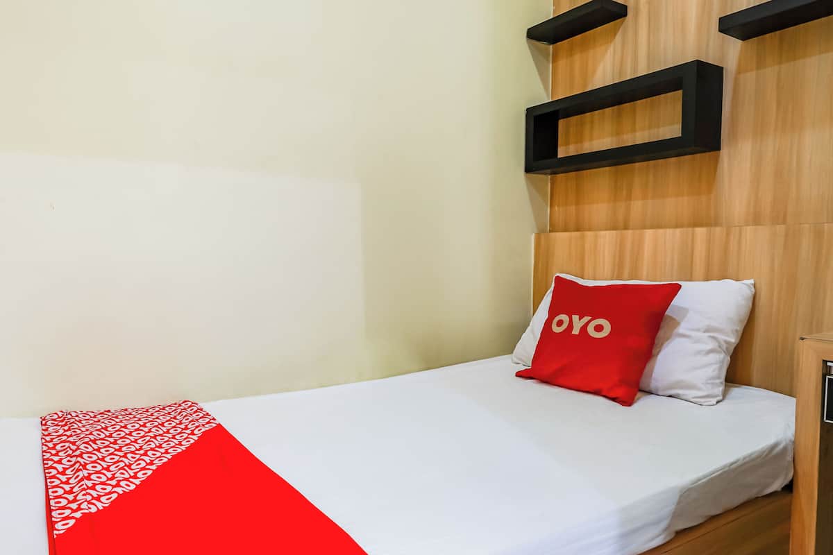 Una cama individual con una colcha blanca y roja, un almohadón rojo con la palabra 