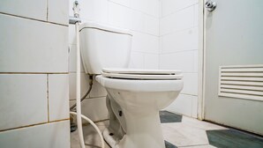 Un inodoro blanco en un baño con paredes de azulejos y una puerta.