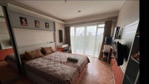 Un dormitorio con cama, escritorio, silla, televisión y ventana con cortinas.