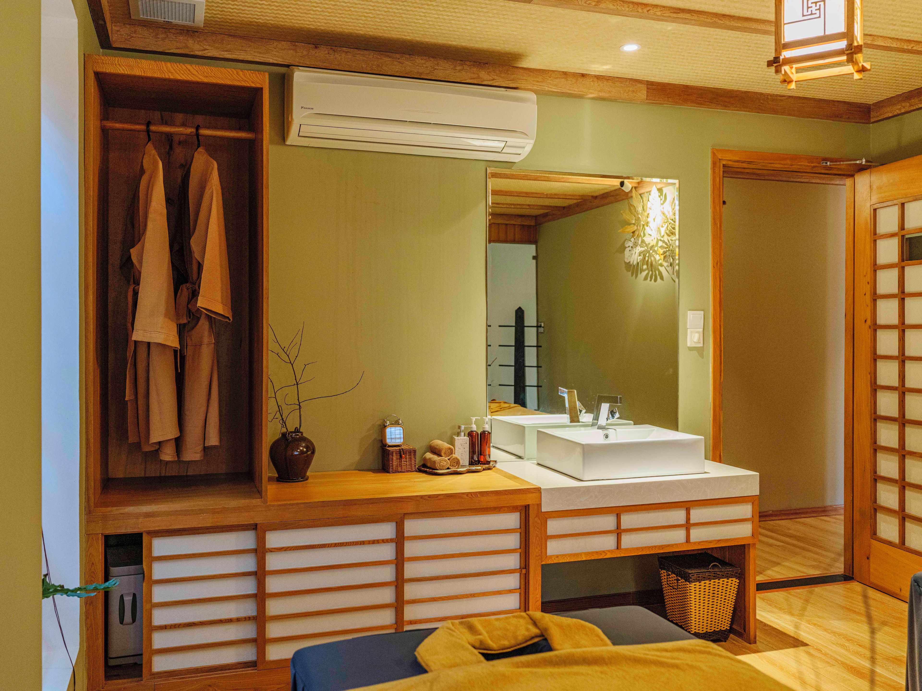 A room with a wooden vanity, a mirror, a bed, and a wall-mounted air conditioner.