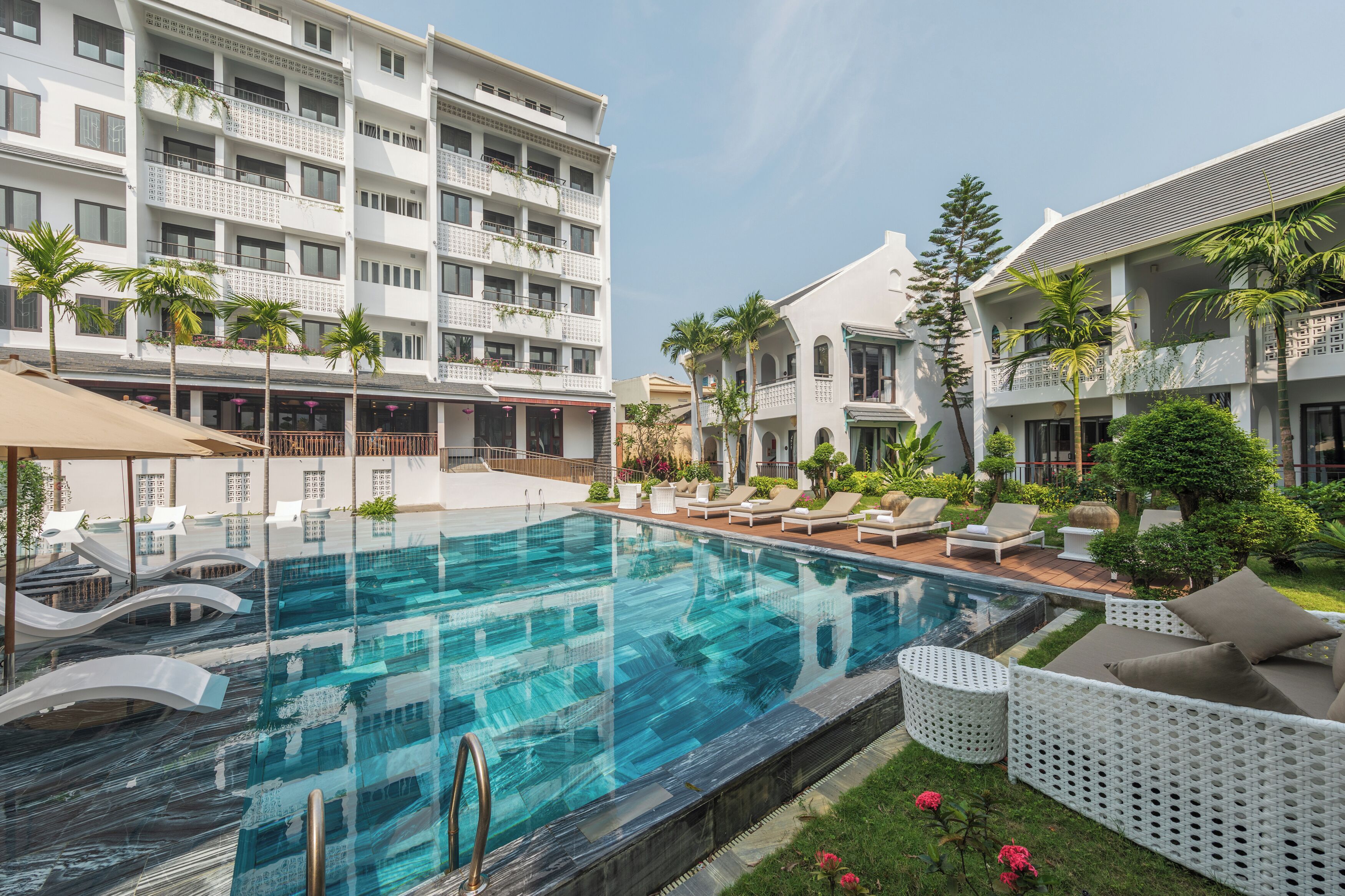 A hotel with a swimming pool, lounge chairs, and a garden area.