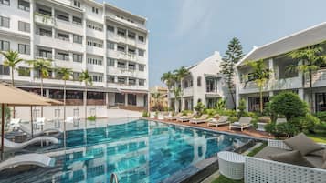 A hotel with a swimming pool, lounge chairs, and a garden area.