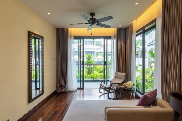 A modern hotel room with a large balcony, a ceiling fan, and a seating area with a table and flowers. - The Saga Hotel Hoi An (Da Nang)