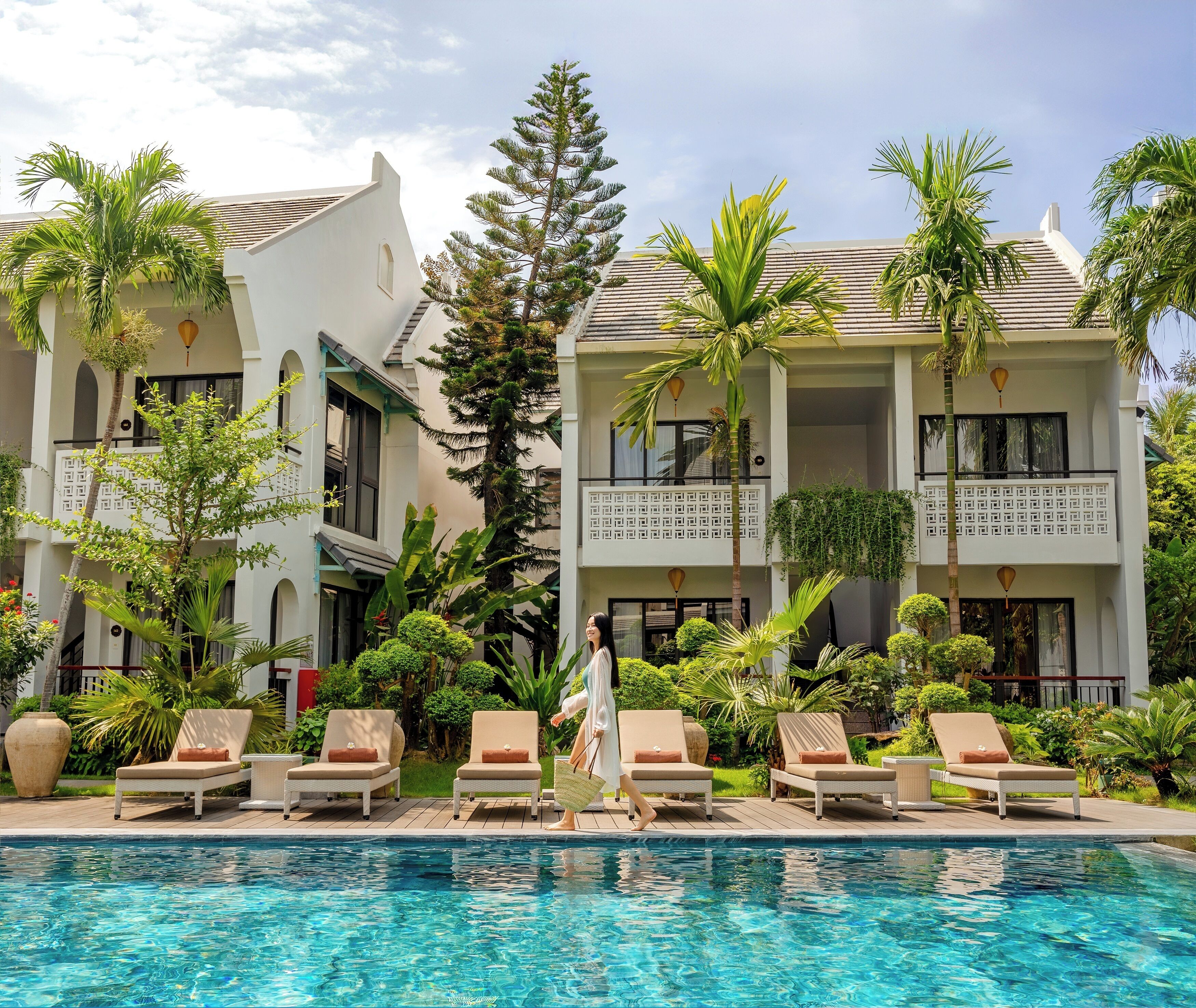 Un resort con piscina, sillones de descanso y plantas tropicales.