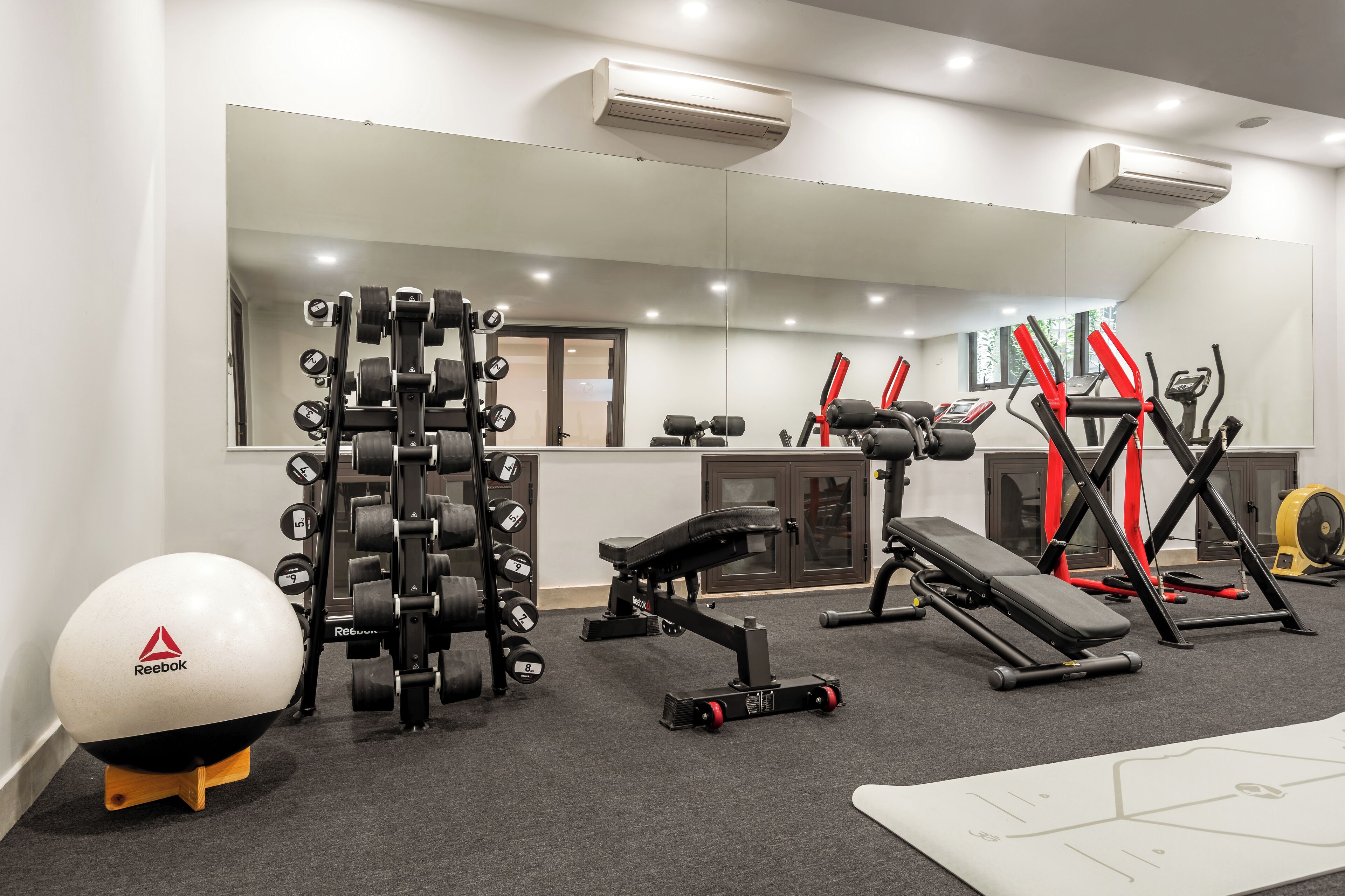 A gym with weightlifting equipment, a bench, and a Reebok exercise ball.