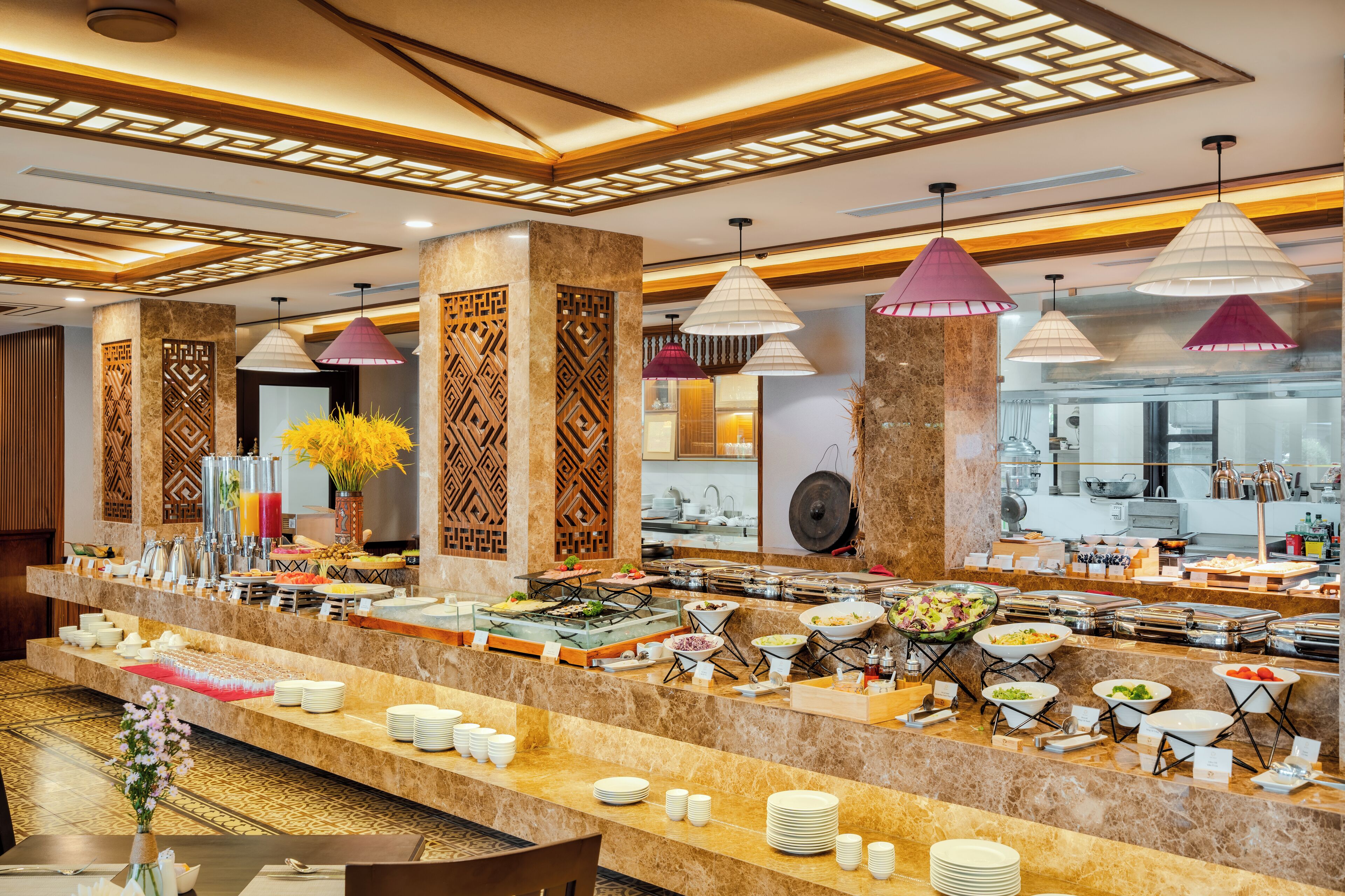 A buffet area with multiple food stations, a kitchen in the background, and decorative lighting.