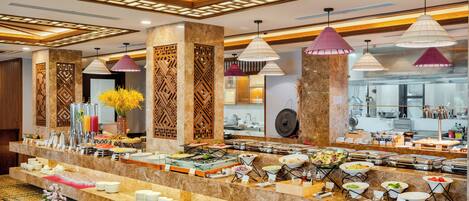 A buffet area with multiple food stations, a kitchen in the background, and decorative lighting.