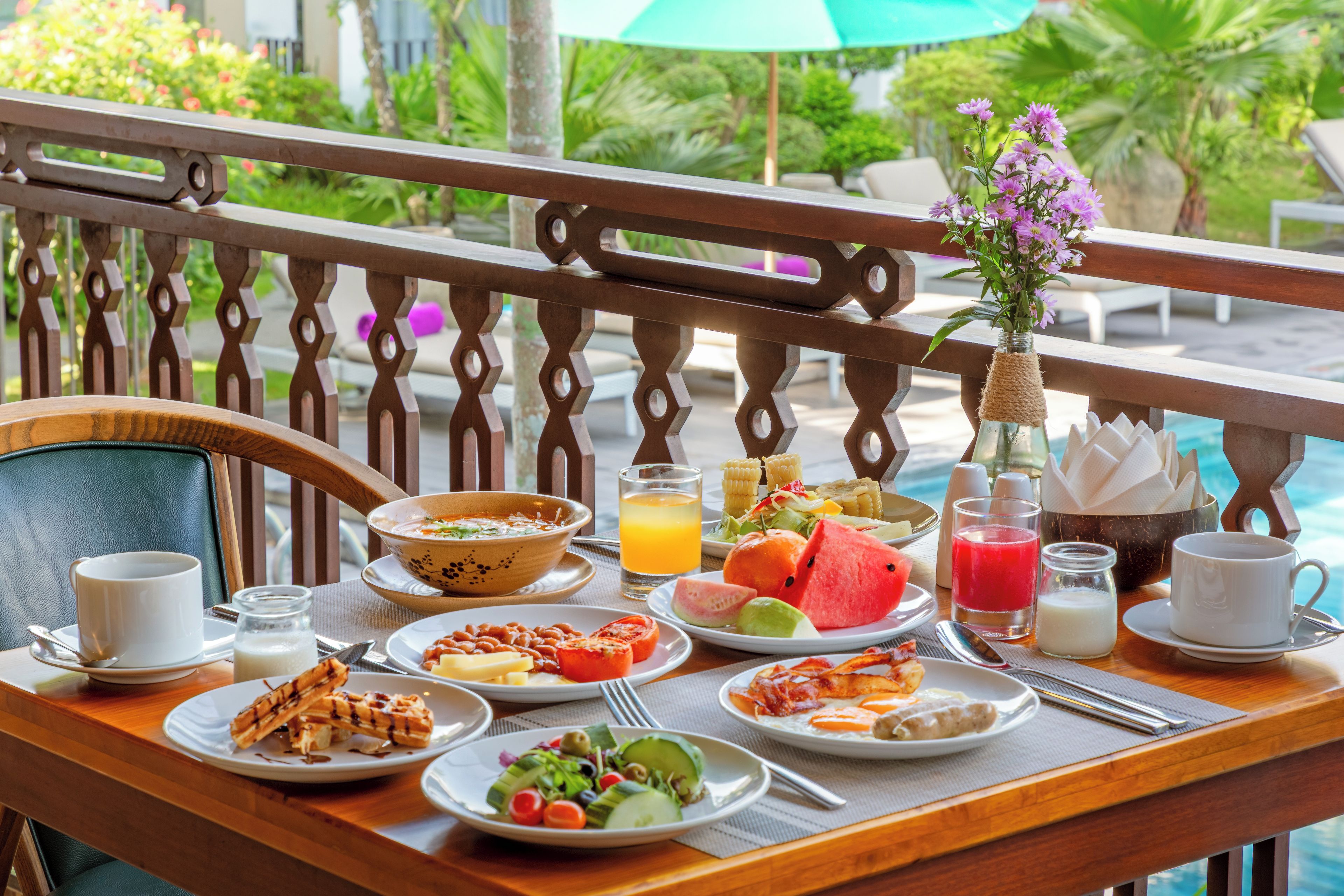 A breakfast table with plates of food, a bowl, a glass of orange juice, a bottle of milk, and a vase with flowers.