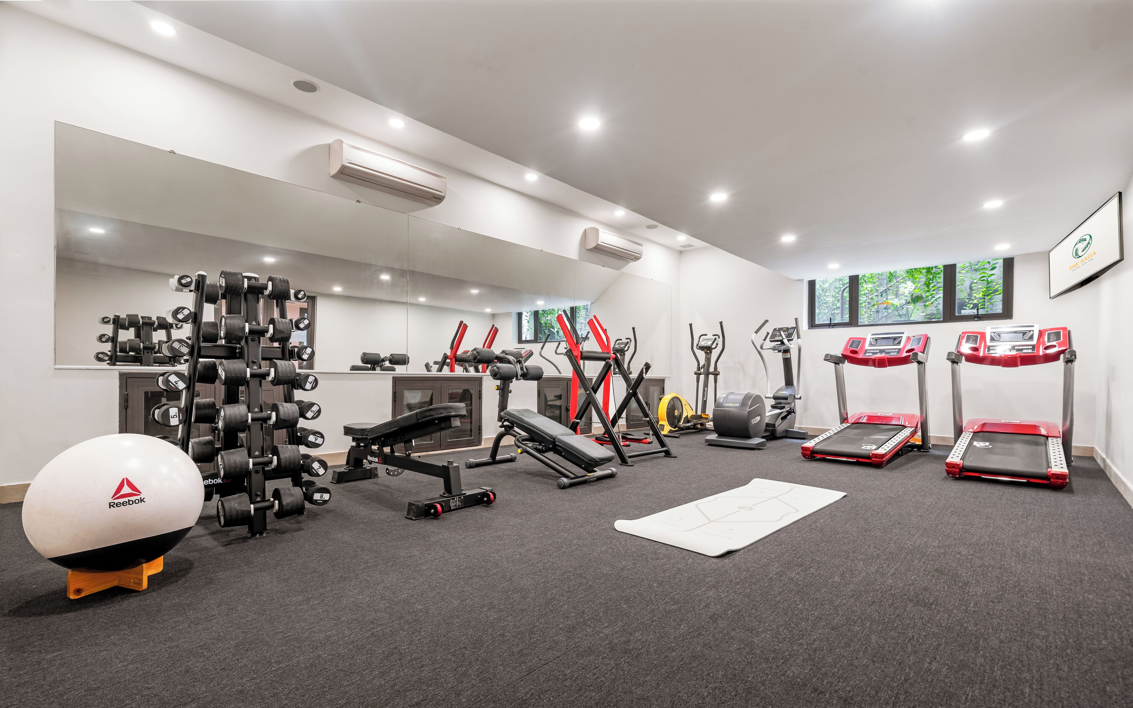 A modern gym with various exercise equipment, including treadmills, a bench press, and dumbbells.