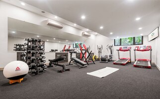 A modern gym with various exercise equipment, including treadmills, a bench press, and dumbbells.