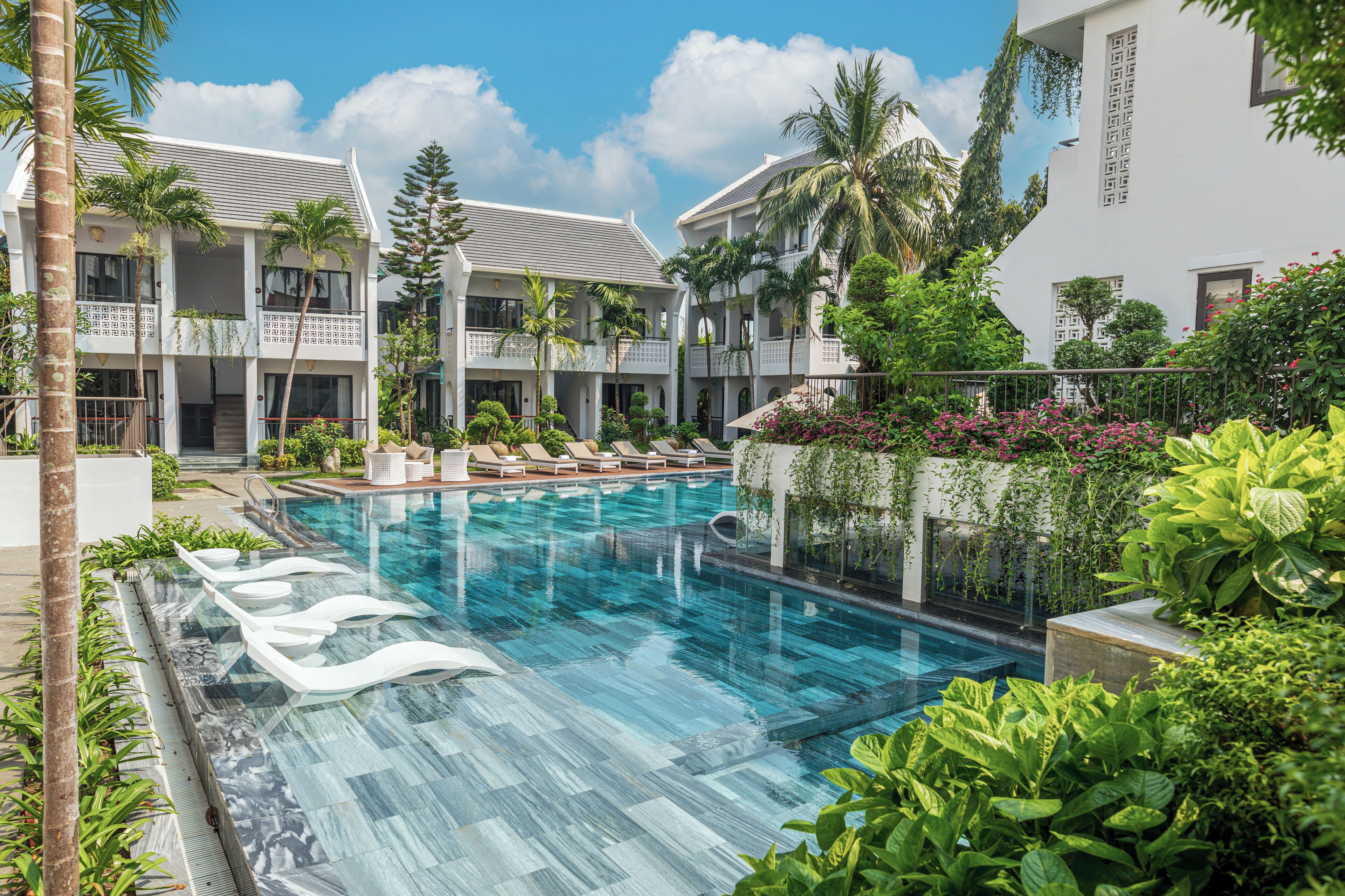 Un hôtel doté d’une piscine, de palmiers et d’un jardin bien entretenu.